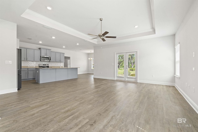 unfurnished living room with a raised ceiling, ceiling fan, crown molding, and wood-type flooring