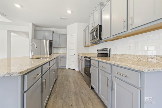 kitchen featuring sink, stainless steel appliances, tasteful backsplash, hardwood / wood-style floors, and gray cabinets