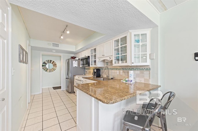 kitchen featuring light stone counters, light tile patterned floors, a sink, tasteful backsplash, and appliances with stainless steel finishes