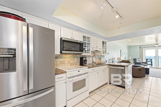 kitchen with white cabinets, stainless steel appliances, a sink, open floor plan, and glass insert cabinets