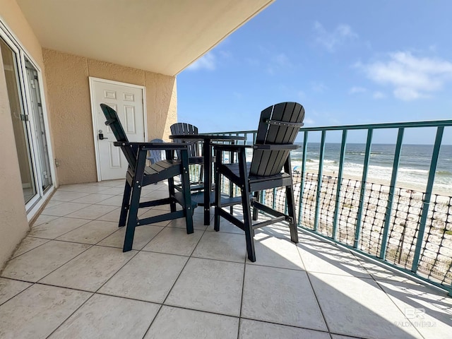 balcony with outdoor dining area, a view of the beach, and a water view
