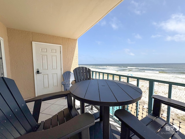 balcony featuring a beach view, outdoor dining space, and a water view