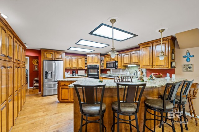 kitchen featuring a skylight, decorative light fixtures, light wood-type flooring, appliances with stainless steel finishes, and kitchen peninsula