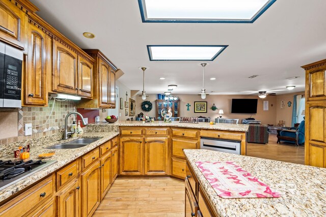 kitchen with light wood-type flooring, a skylight, decorative light fixtures, kitchen peninsula, and sink