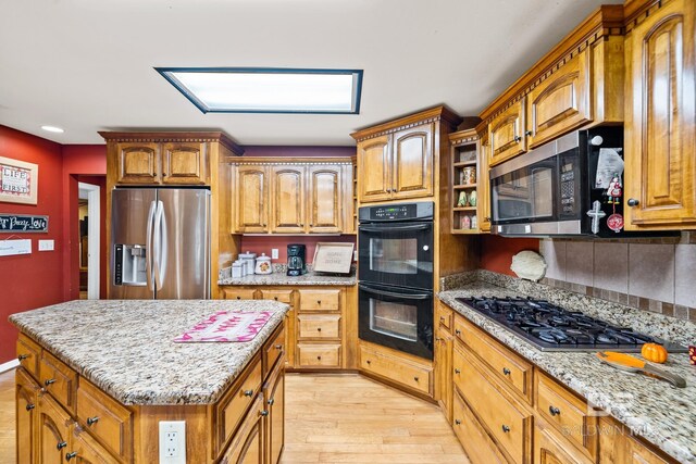 kitchen featuring light wood-type flooring, appliances with stainless steel finishes, a kitchen island, and light stone countertops