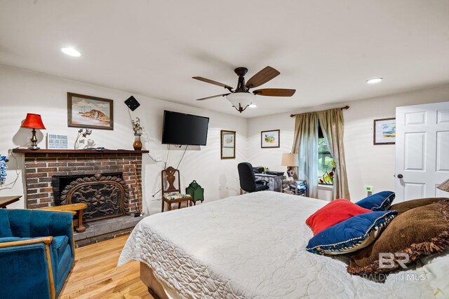 bedroom with a brick fireplace, wood-type flooring, and ceiling fan