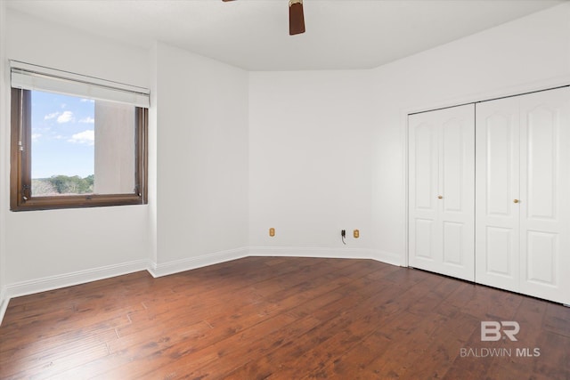 unfurnished bedroom with a closet, dark wood-style flooring, baseboards, and a ceiling fan