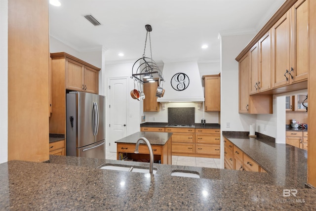 kitchen with sink, stainless steel fridge, dark stone countertops, hanging light fixtures, and custom exhaust hood