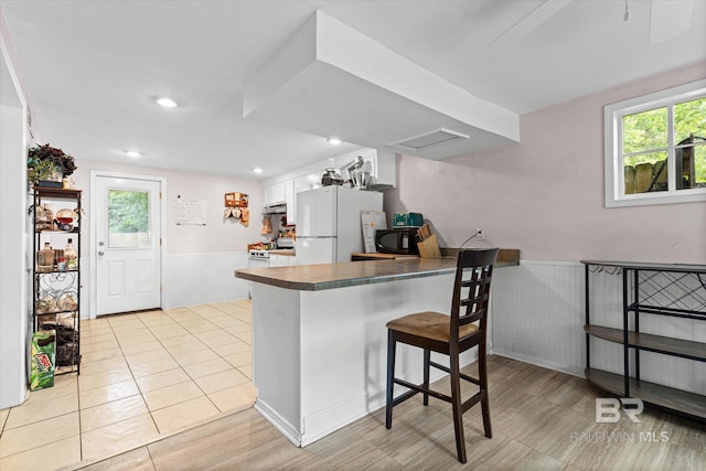 162 Westwood St, Mobile, AL 36606 - kitchen with white appliances, a peninsula, a wainscoted wall, white cabinets, and under cabinet range hood