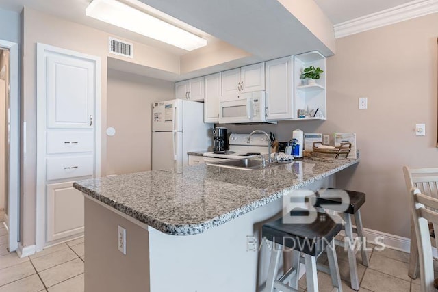 kitchen featuring white appliances, white cabinets, a breakfast bar area, kitchen peninsula, and light tile floors