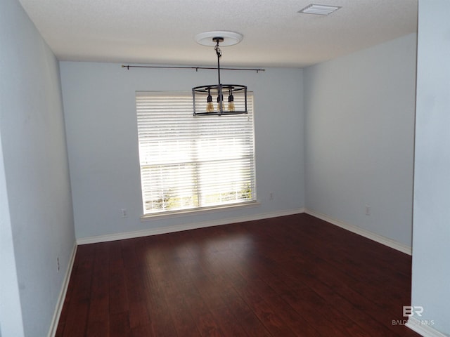 unfurnished room featuring a notable chandelier, dark wood-type flooring, visible vents, and baseboards