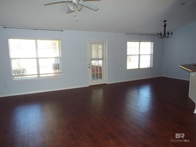 unfurnished living room with ceiling fan with notable chandelier, dark wood-style flooring, and baseboards