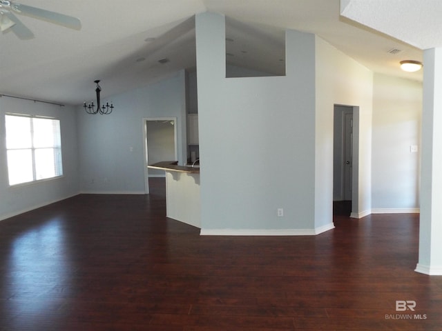 unfurnished living room featuring dark wood-type flooring, vaulted ceiling, baseboards, and ceiling fan with notable chandelier