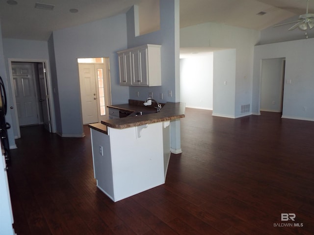 kitchen featuring a breakfast bar area, lofted ceiling, visible vents, white cabinetry, and a peninsula