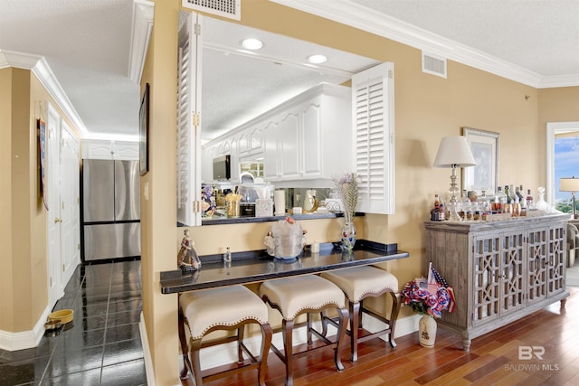 bar featuring visible vents, freestanding refrigerator, baseboards, and ornamental molding