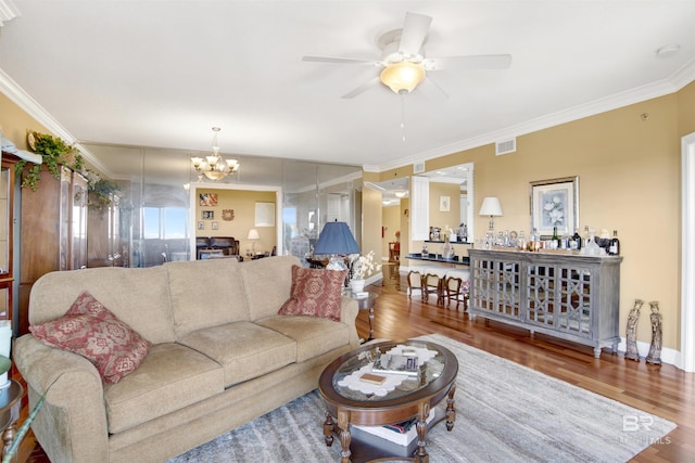 living room with visible vents, ceiling fan with notable chandelier, crown molding, and wood finished floors