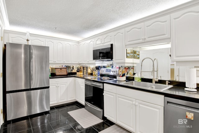 kitchen with dark countertops, white cabinets, a sink, appliances with stainless steel finishes, and granite finish floor