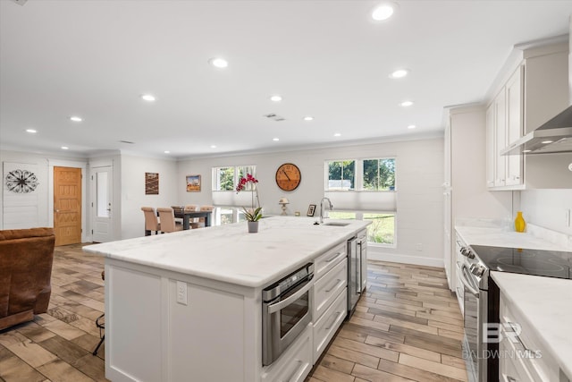 kitchen with light stone countertops, crown molding, white cabinetry, light hardwood / wood-style flooring, and a center island with sink