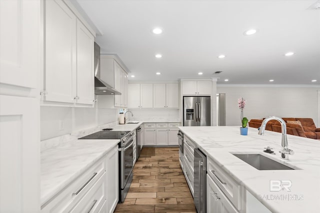 kitchen with stainless steel appliances, white cabinets, sink, wall chimney range hood, and ornamental molding