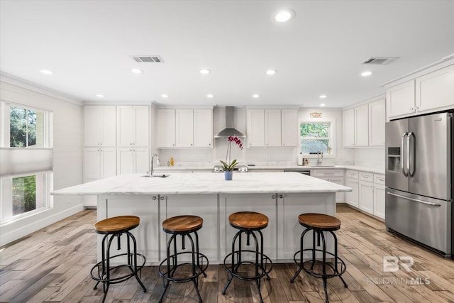 kitchen featuring a center island with sink, plenty of natural light, wall chimney range hood, and stainless steel appliances