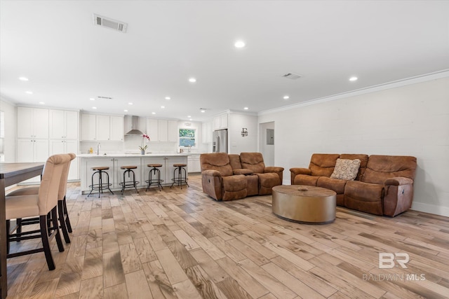 living room featuring light hardwood / wood-style floors, ornamental molding, and sink