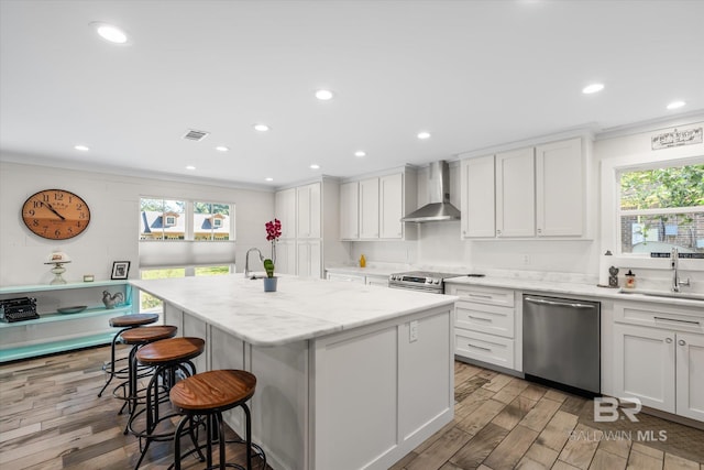 kitchen featuring appliances with stainless steel finishes, plenty of natural light, wall chimney range hood, and a kitchen island with sink