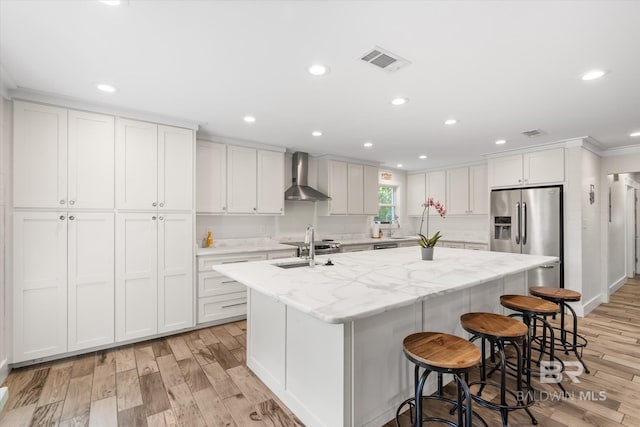 kitchen featuring a kitchen island with sink, wall chimney exhaust hood, light hardwood / wood-style floors, and white cabinetry