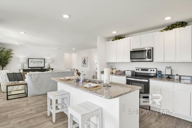 kitchen featuring an island with sink, sink, white cabinets, stainless steel appliances, and light stone countertops