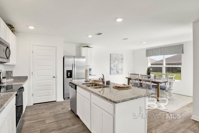 kitchen with sink, a kitchen island with sink, stainless steel appliances, light stone counters, and white cabinets