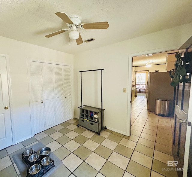 interior space with light tile patterned floors, visible vents, a ceiling fan, a closet, and freestanding refrigerator