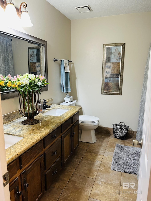 bathroom featuring toilet, double vanity, a sink, and visible vents