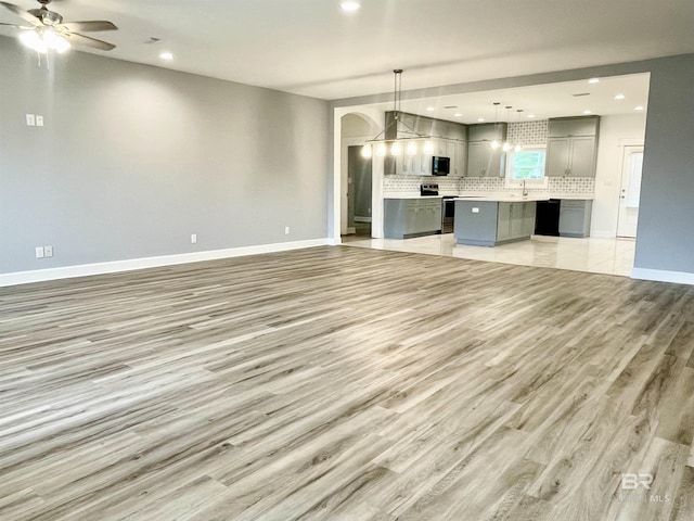 unfurnished living room with ceiling fan, sink, and light hardwood / wood-style flooring