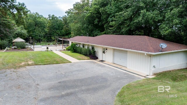 ranch-style house featuring aphalt driveway, an attached garage, a front yard, and a shingled roof