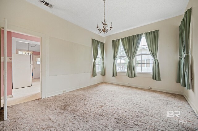 spare room with carpet floors, a chandelier, and a textured ceiling