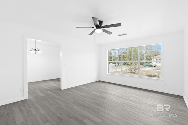 empty room with ceiling fan with notable chandelier and dark hardwood / wood-style floors