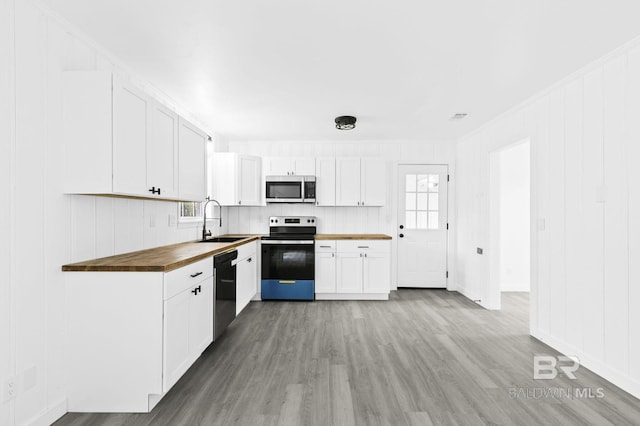 kitchen with stainless steel appliances, butcher block counters, light hardwood / wood-style floors, white cabinets, and sink