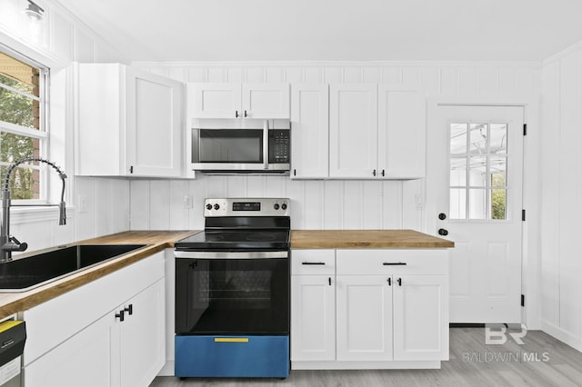 kitchen featuring stainless steel appliances, sink, white cabinets, butcher block countertops, and a wealth of natural light