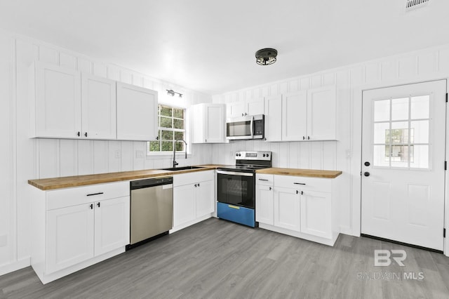 kitchen featuring white cabinetry, appliances with stainless steel finishes, butcher block countertops, sink, and light hardwood / wood-style flooring