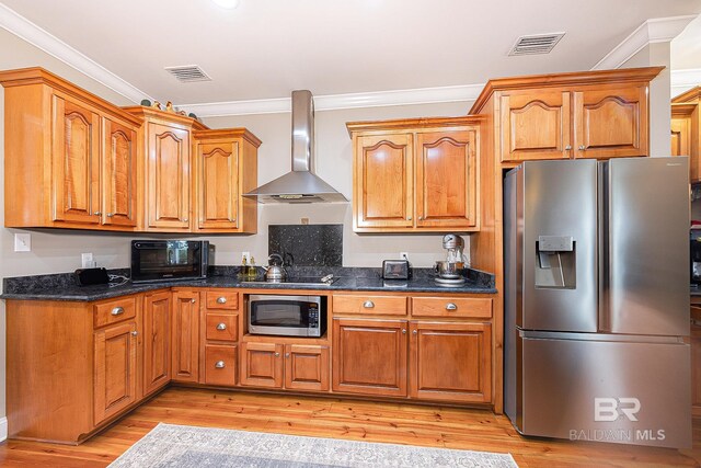 kitchen featuring light hardwood / wood-style flooring, stainless steel appliances, ornamental molding, dark stone countertops, and wall chimney range hood