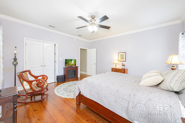 bedroom with a closet, wood-type flooring, crown molding, and ceiling fan