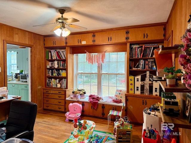 interior space featuring crown molding, ceiling fan, wooden walls, and light hardwood / wood-style flooring