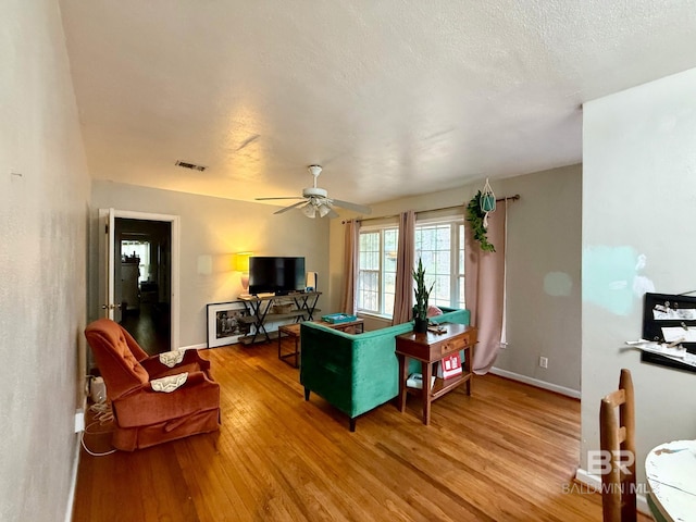 living room featuring ceiling fan, light hardwood / wood-style floors, and a textured ceiling