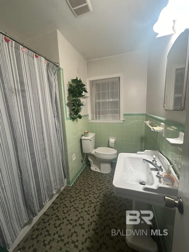 bathroom with walk in shower, toilet, sink, and tile walls