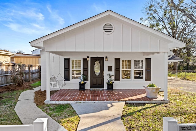 view of front of home with board and batten siding, covered porch, and fence