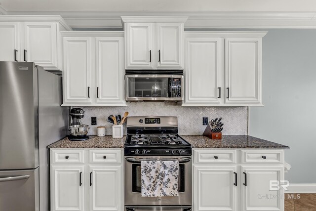 kitchen with stainless steel appliances, tasteful backsplash, white cabinets, dark stone countertops, and baseboards