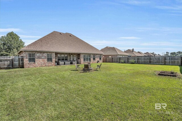 back of house featuring a fenced backyard, a fire pit, brick siding, a shingled roof, and a lawn