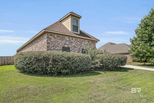 view of side of property with roof with shingles, brick siding, a yard, and fence