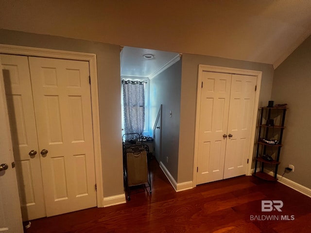 unfurnished bedroom with crown molding, dark wood-type flooring, multiple closets, and lofted ceiling