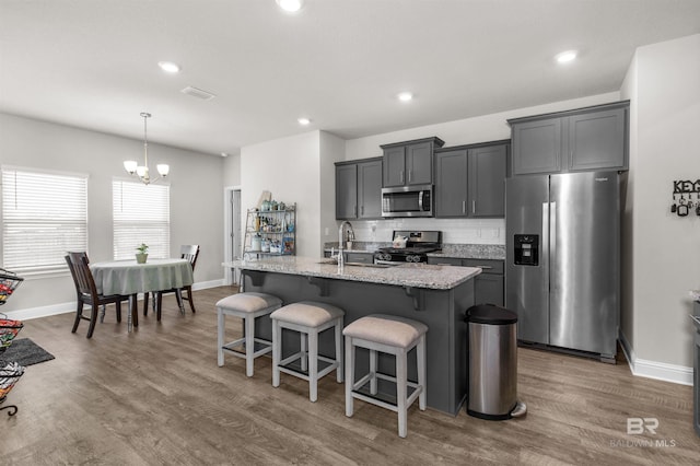 2345 Laurel St, Semmes, AL 36575 - kitchen with appliances with stainless steel finishes, an island with sink, a kitchen bar, wood finished floors, and light stone counters