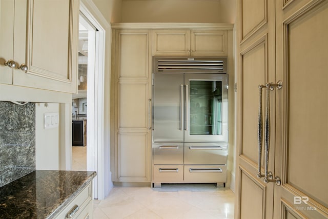 interior space with cream cabinetry, light tile patterned floors, dark stone countertops, and stainless steel built in fridge